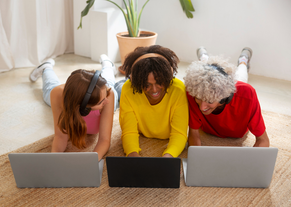 Three young ladies lying on the floor, working together on their laptops and wearing headphones. This image represents the collaborative and engaging environment facilitated by KYG’s tools for effective online community management.