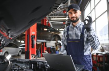 Технічний спеціаліст офіційного Тойота сервіс демонструє професіоналізм і готовність до роботи, стоячи біля автомобіля під час технічного обслуговування.